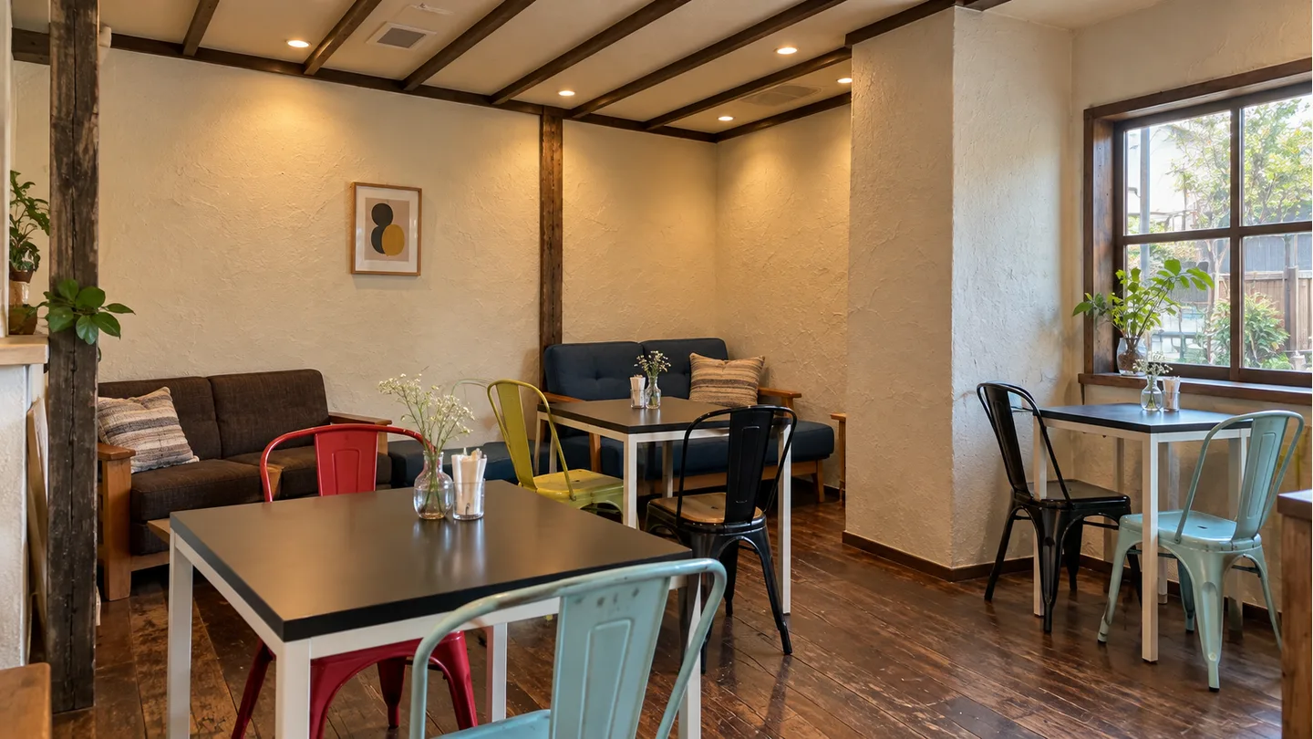 木の梁とソファ席、色の異なる椅子があるカフェの店内